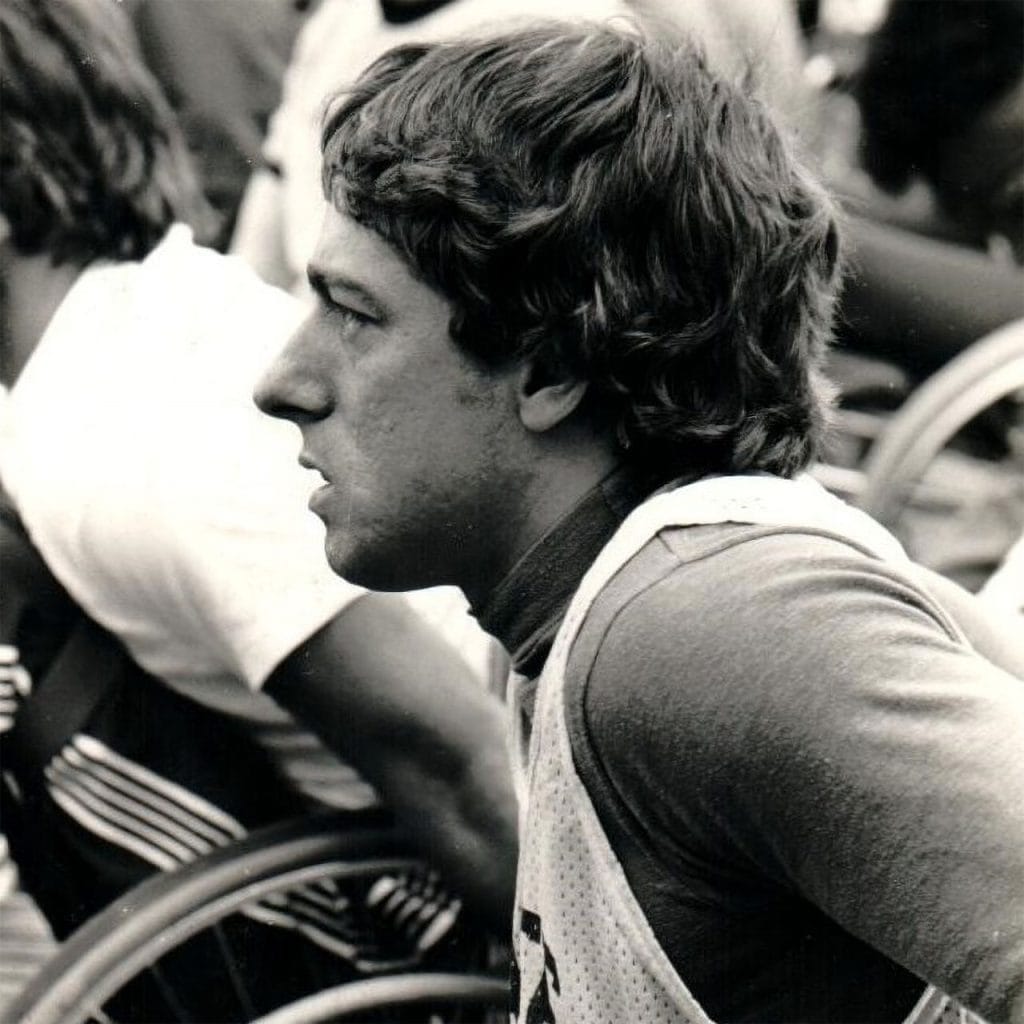 Bob Hall in profile during a wheelchair racing event in the 1970s, focused and preparing to push forward.